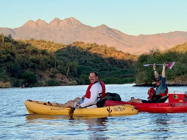 Two people kayaking on a river with mountains in the background