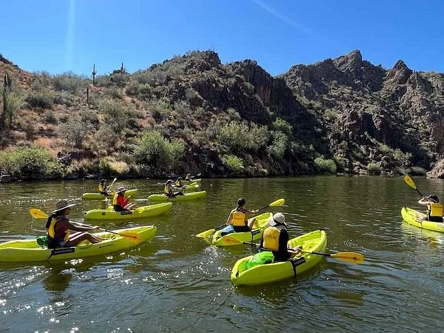 A group of people kayaking on a lake near a rocky hillside