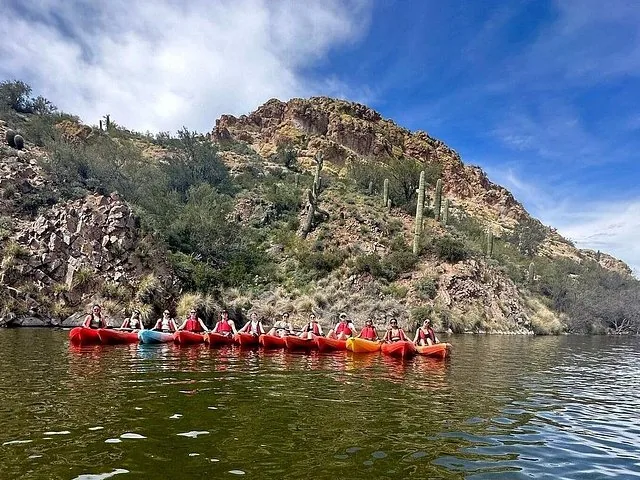 A large group of kayakers lined up side-by-side on a calm lake