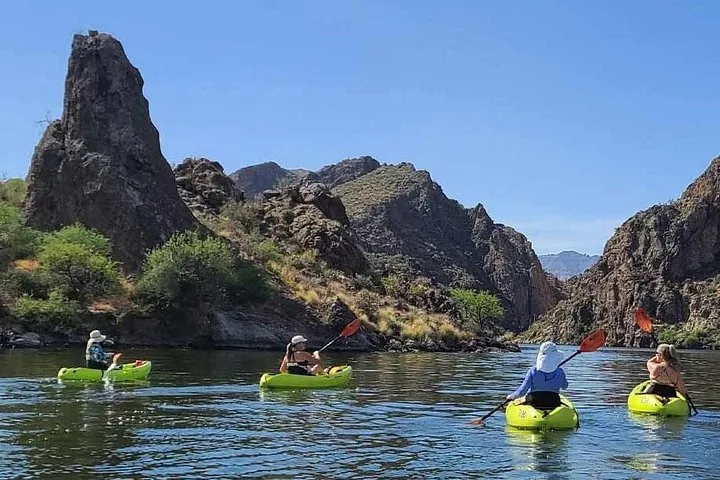 People kayaking on a wide river with rocky cliffs in the background