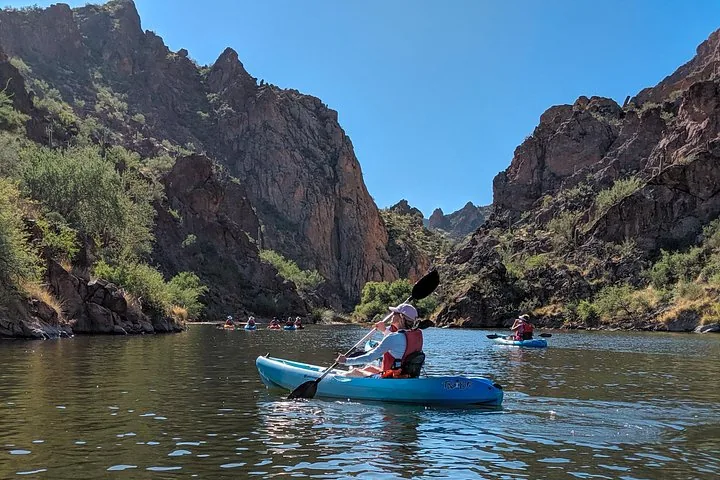 Group kayaking through a canyon with rocky walls on a sunny day