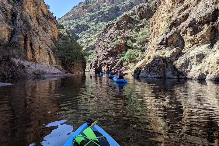Kayakers paddle through a narrow canyon on a calm river