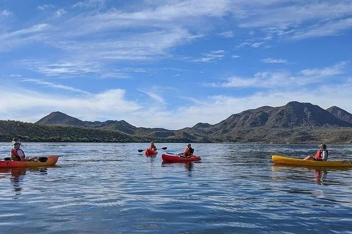 Four people kayaking on a wide lake with mountains in the distance