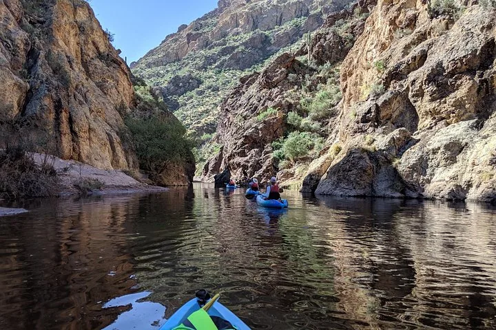 Kayakers paddle through a narrow canyon on a calm river
