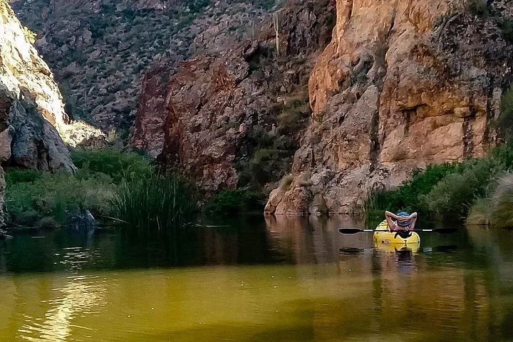 A person relaxes in a yellow kayak on a calm, canyon-lined river